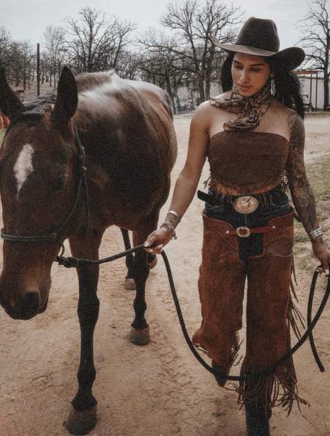 A woman in a cowboy hat leading a horse
